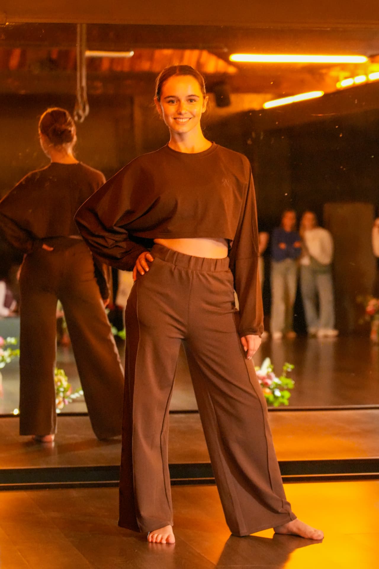 Een model poseert in een bruine korte sweater en wijde bruine broek