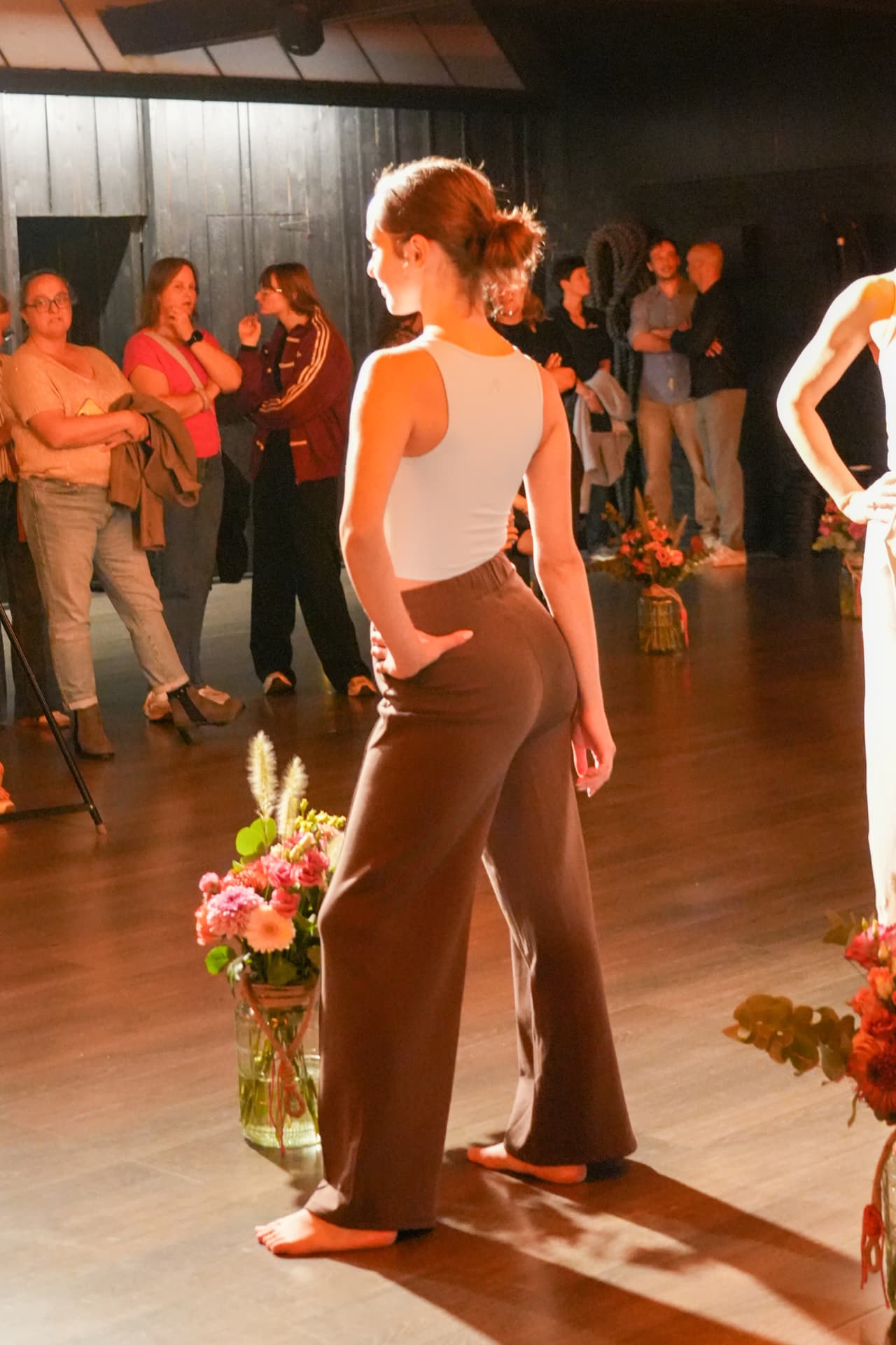 Een model poseert van opzij in een lichtblauwe top en wijde bruine broek