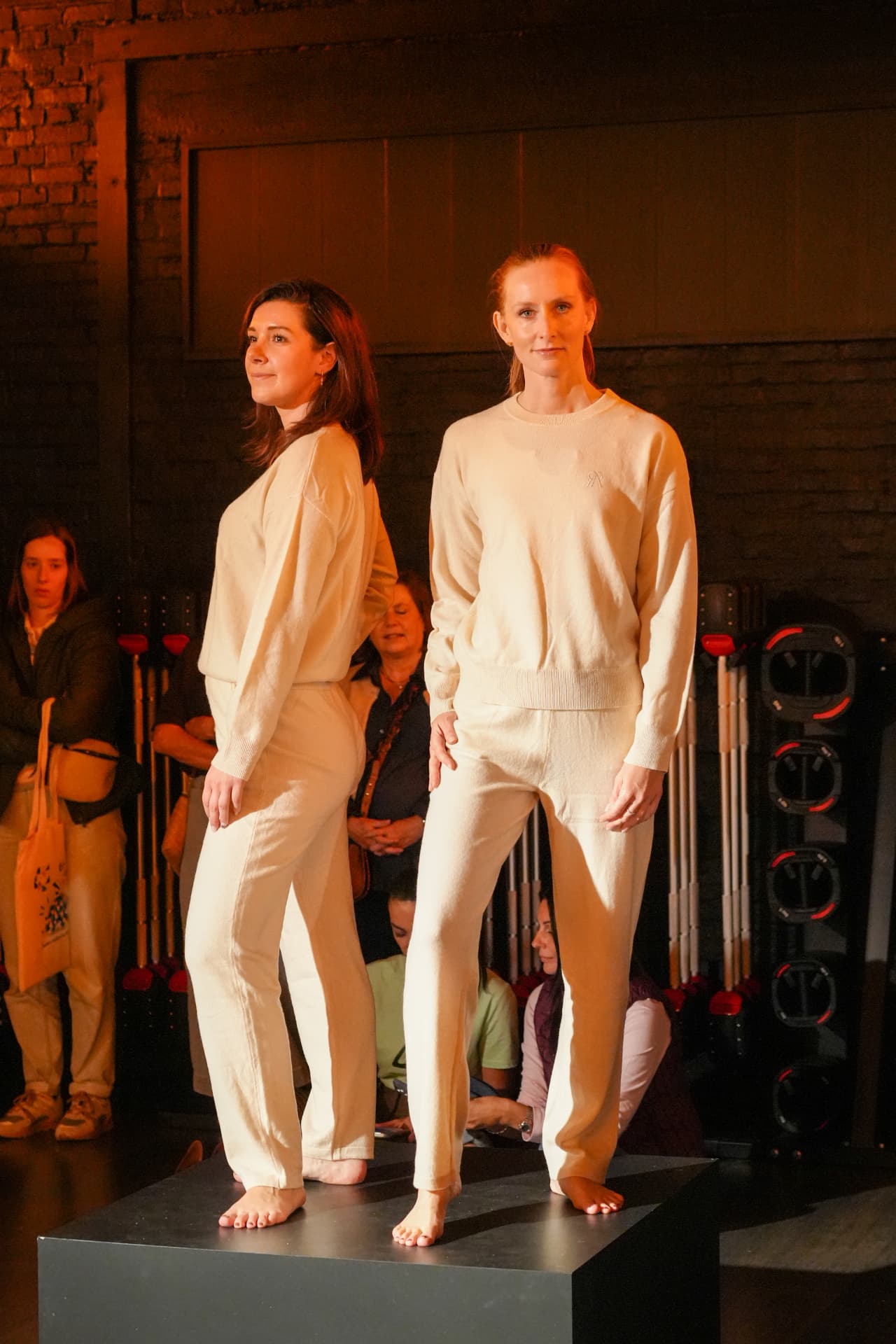 Twee modellen poseren in lichte sweaters en broeken op het podium
