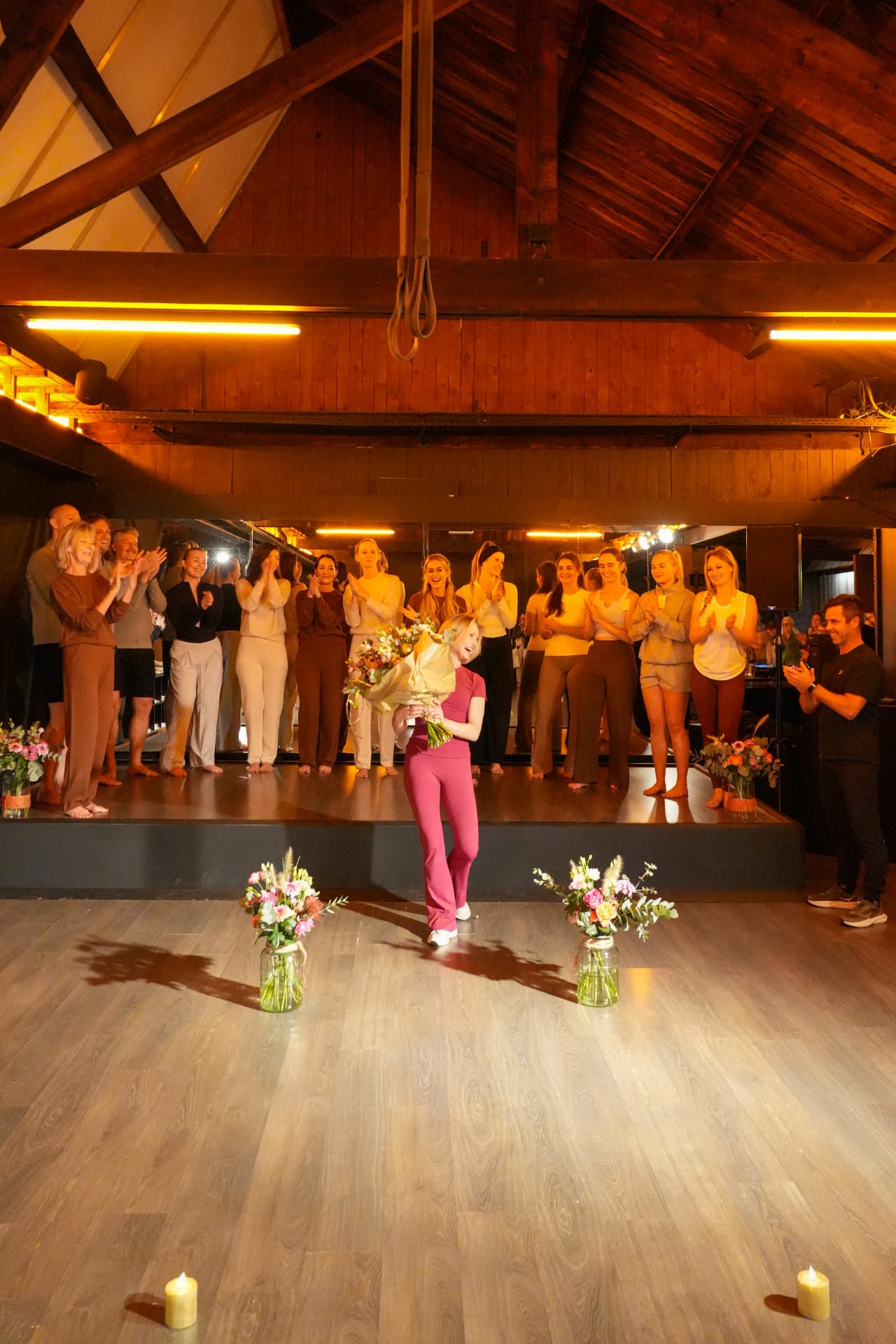 Een vrouw in een bordeauxrode outfit houdt een boeket vast voor het applaudisserende team