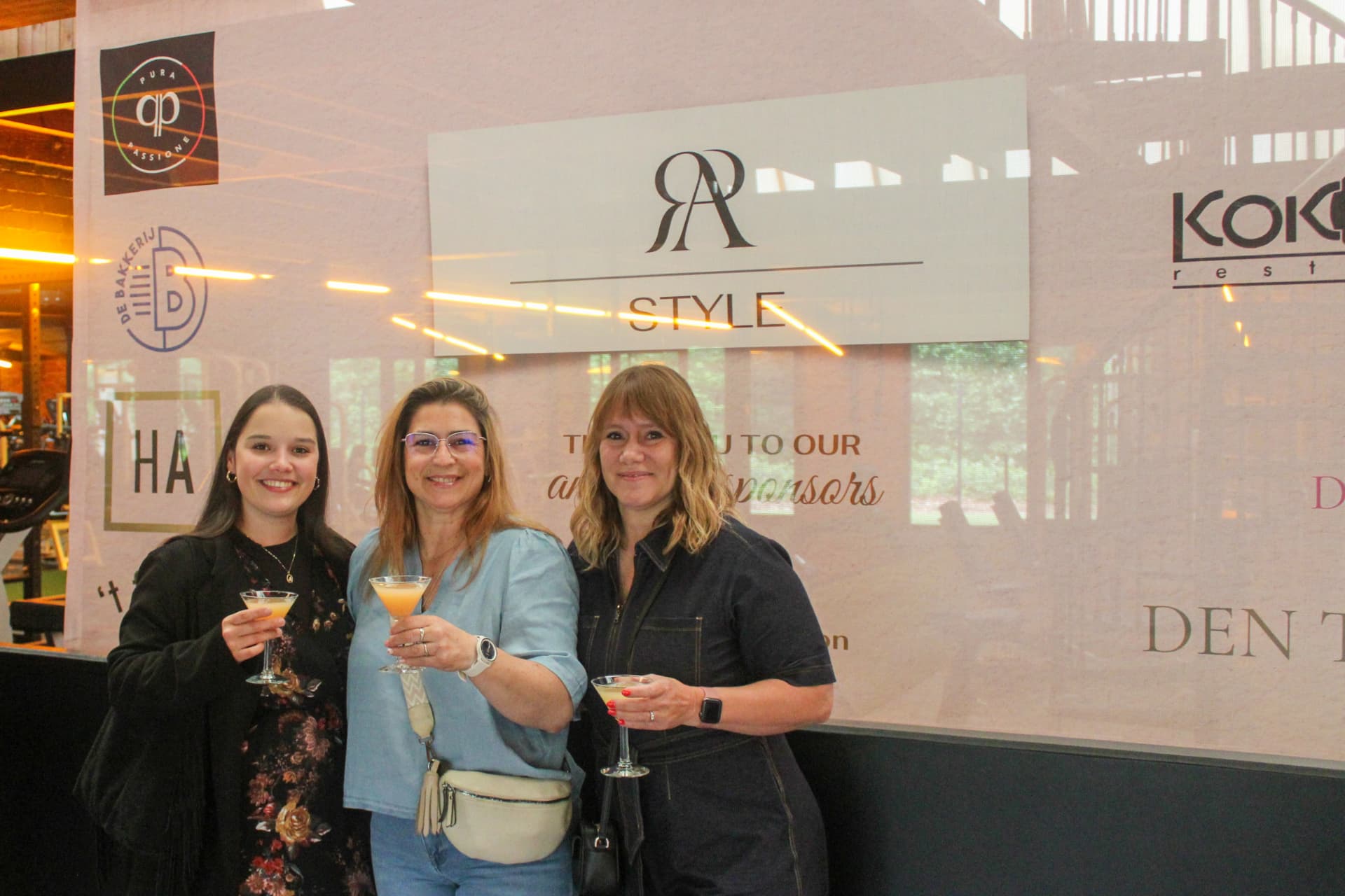 Drie bezoekers poseren met hun drankje voor de RA Style-wand
