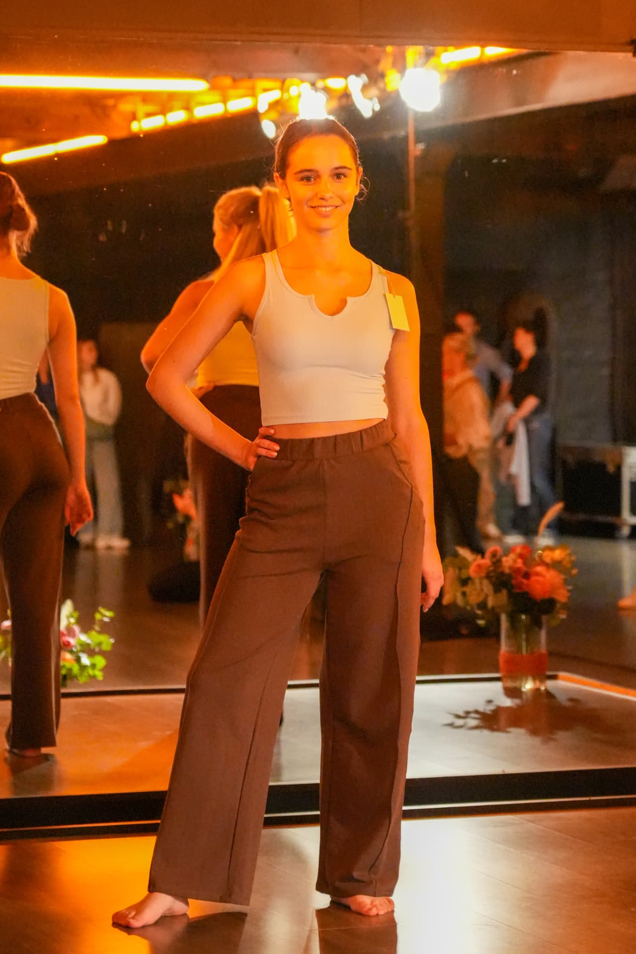 Een model poseert in een lichtblauwe korte top en wijde bruine broek voor de spiegelwand