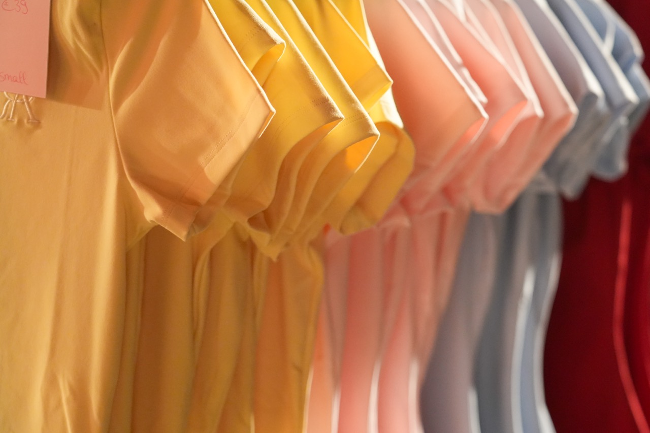Gele, roze en lichtblauwe shirts hangen naast elkaar aan een kledingrek