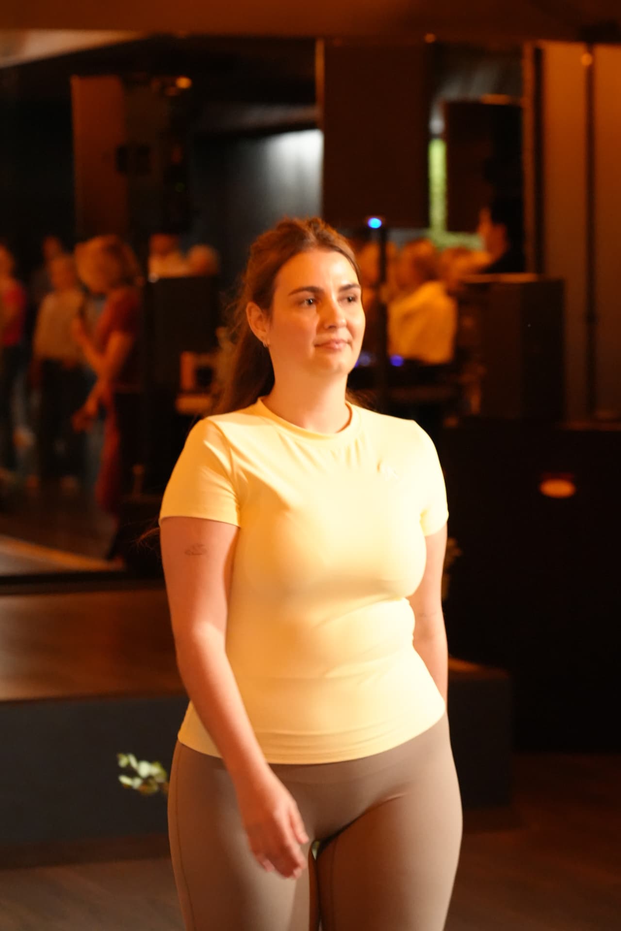Een model wandelt in een gele top en taupekleurige broek
