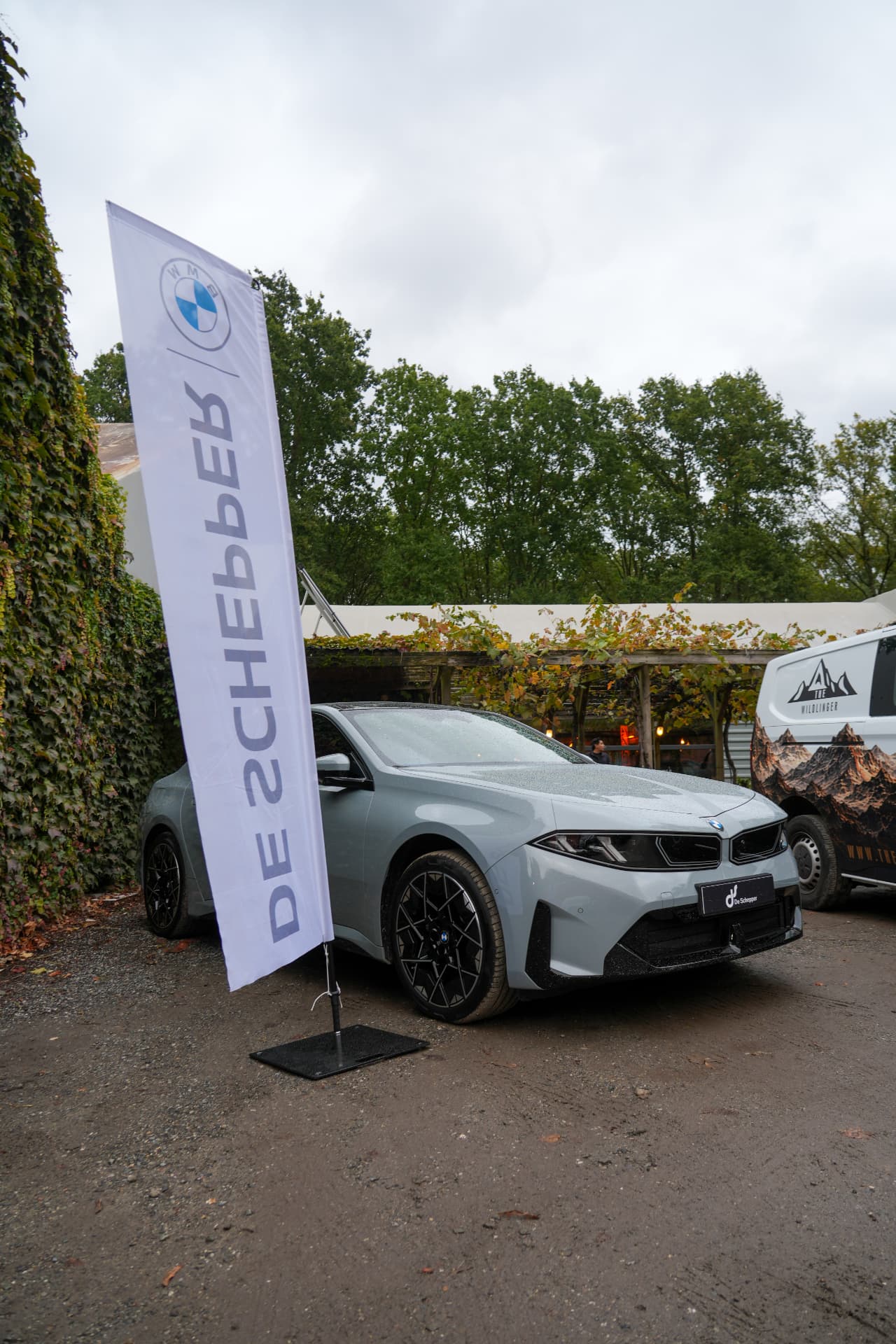 Een glanzende BMW met een BMW-vlag van De Schepper buiten het gebouw