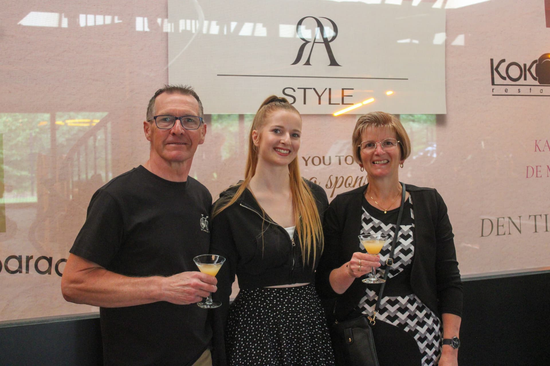 Drie bezoekers klinken met een cocktail voor de RA Style-wand