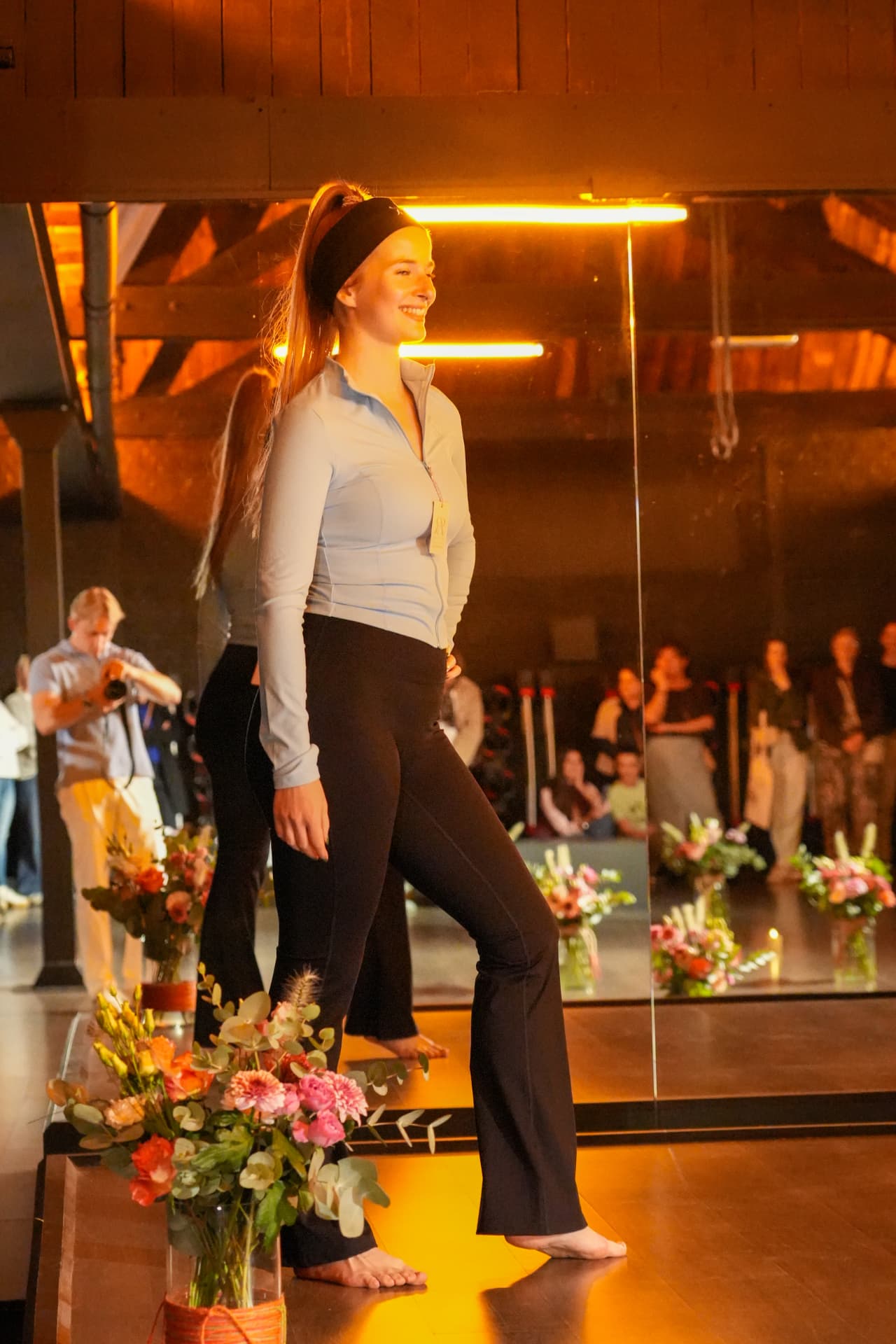Een model toont een lichtblauw sportjasje en zwarte broek bij de bloemen
