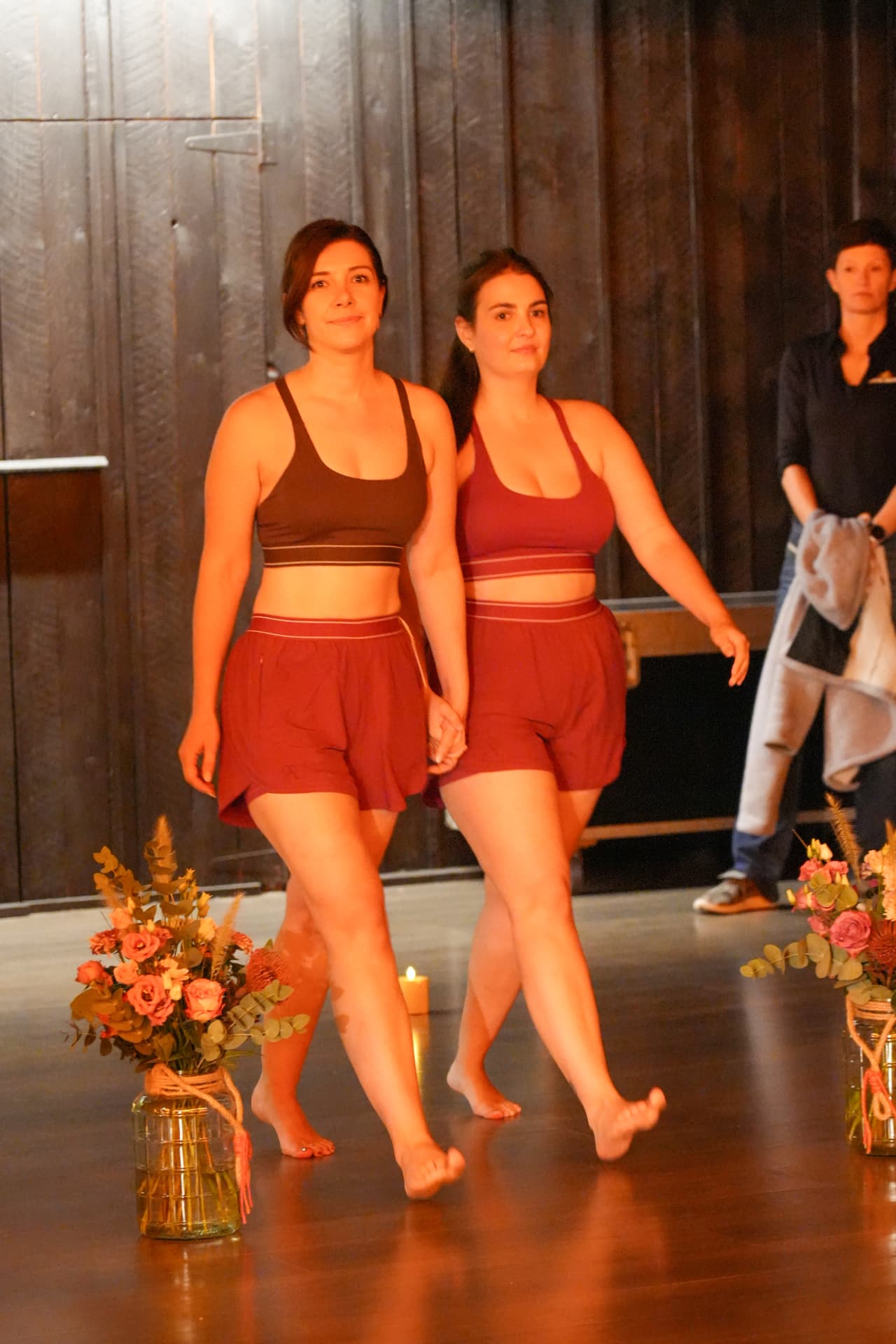 Twee modellen wandelen hand in hand in sporttops en bordeauxrode shorts