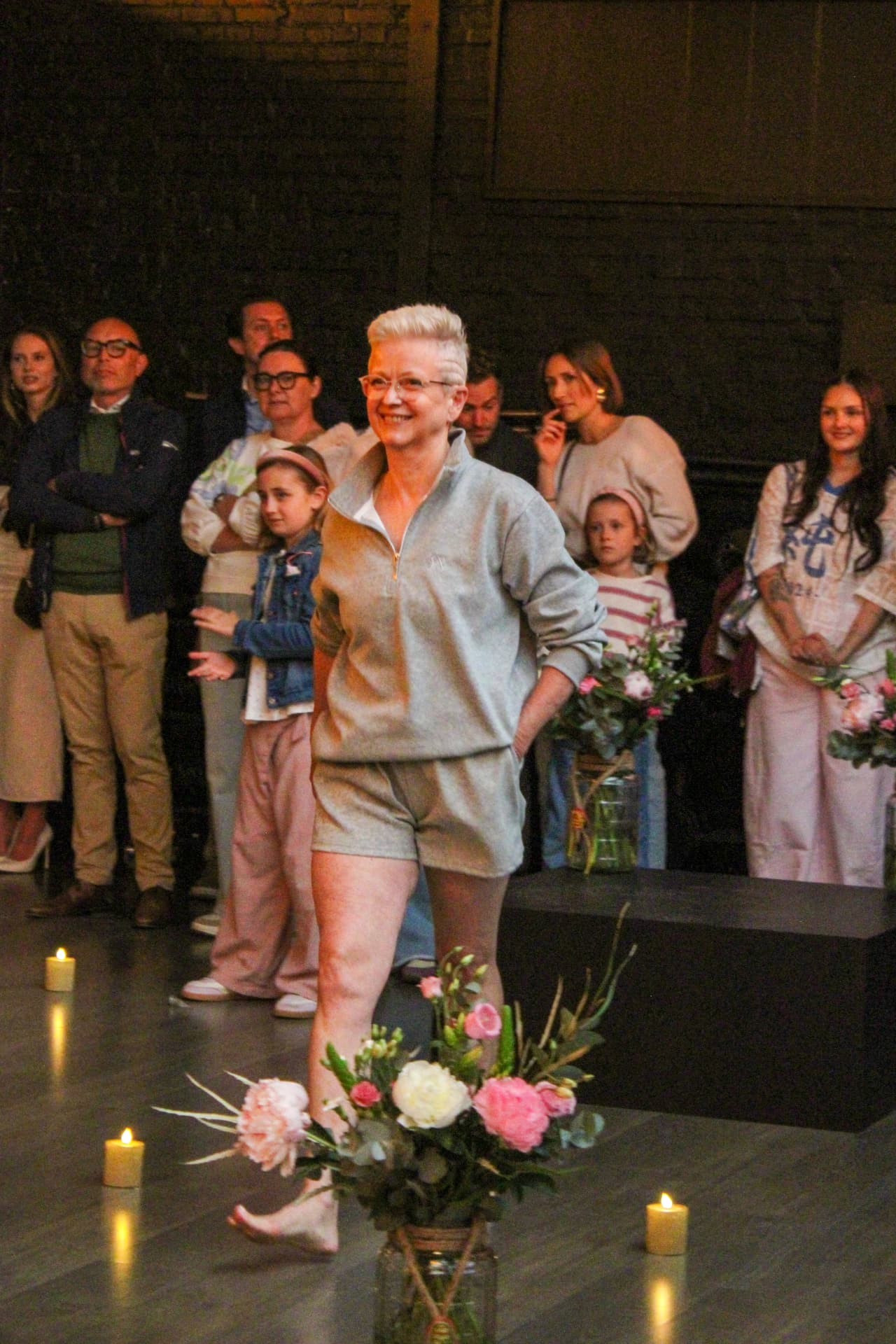 Een model in een grijze sportlook wandelt langs bloemen op de catwalk