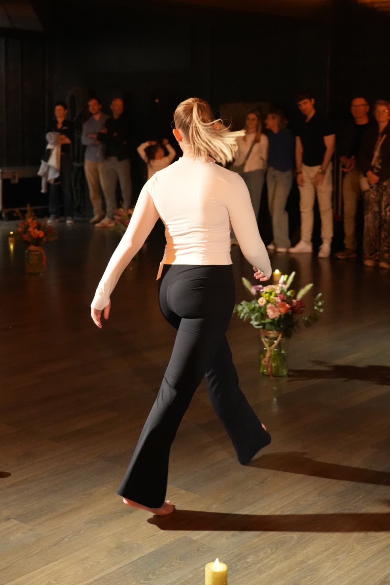 Een model in een lichte top en zwarte broek wandelt met haar rug naar de camera