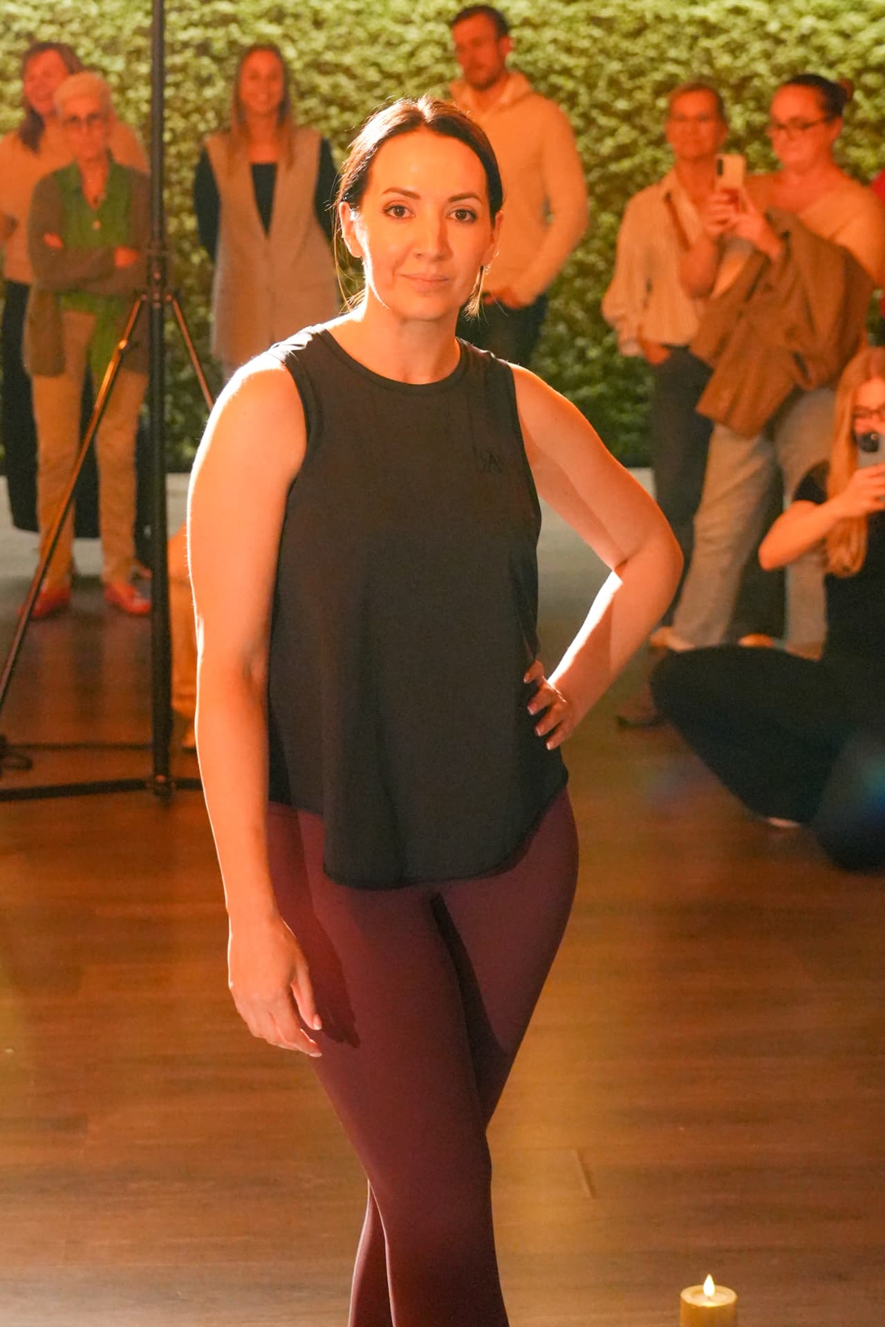Een model poseert in een zwarte mouwloze top en bordeauxrode legging