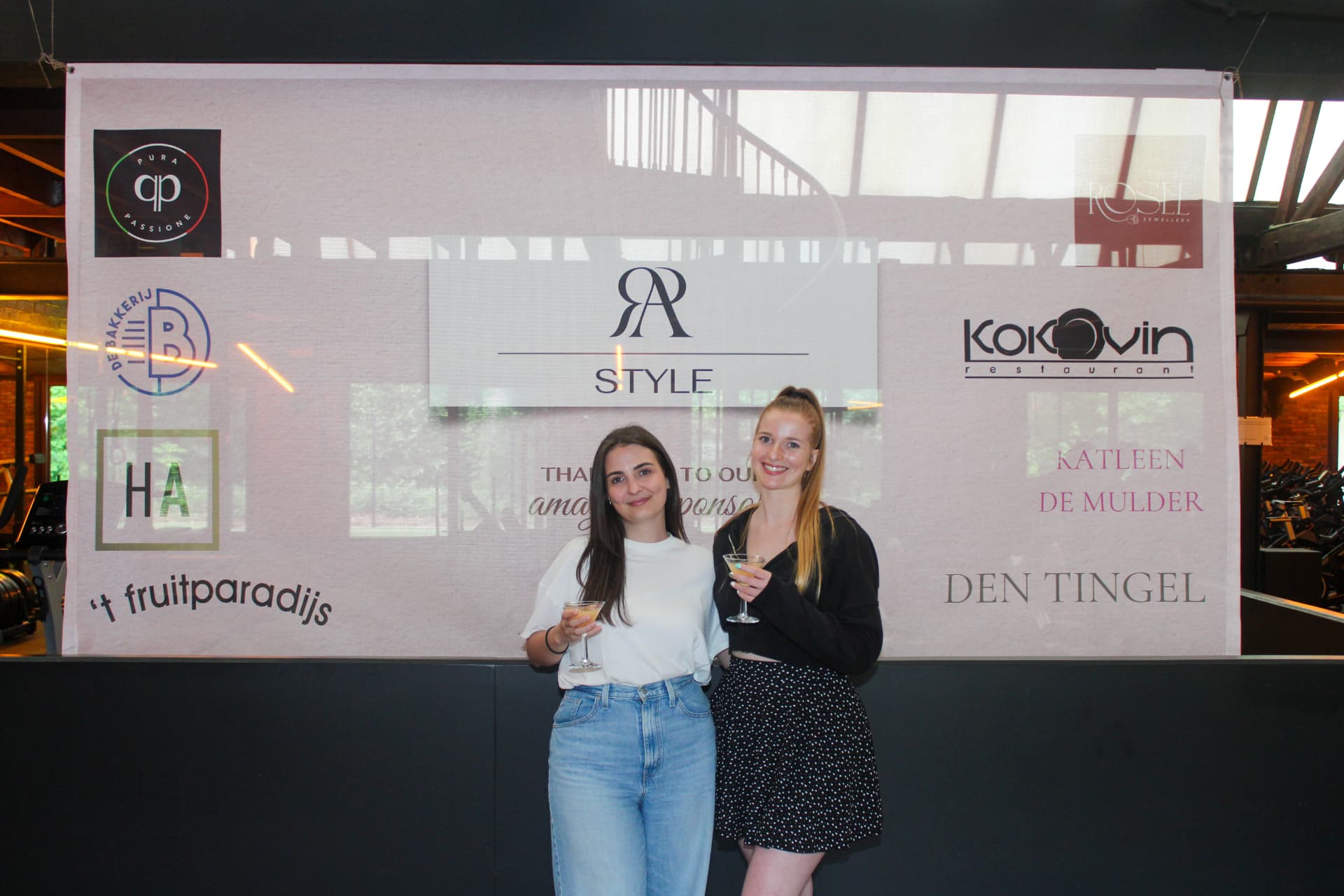 Twee bezoekers met een drankje voor het sponsordoek